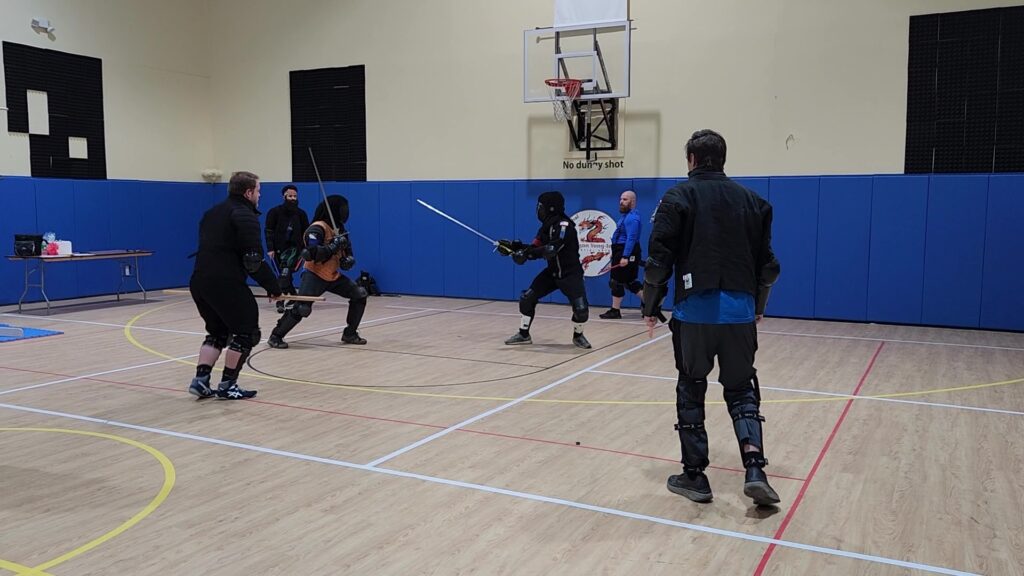 HEMA fighters practicing with swords surrounded by three judges and ref