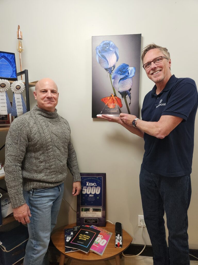Two men smile and one holds a crystal plaque in an office