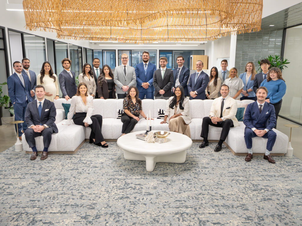 A group of people stand behind a large, corporate sofa while six people sit on the sofa.