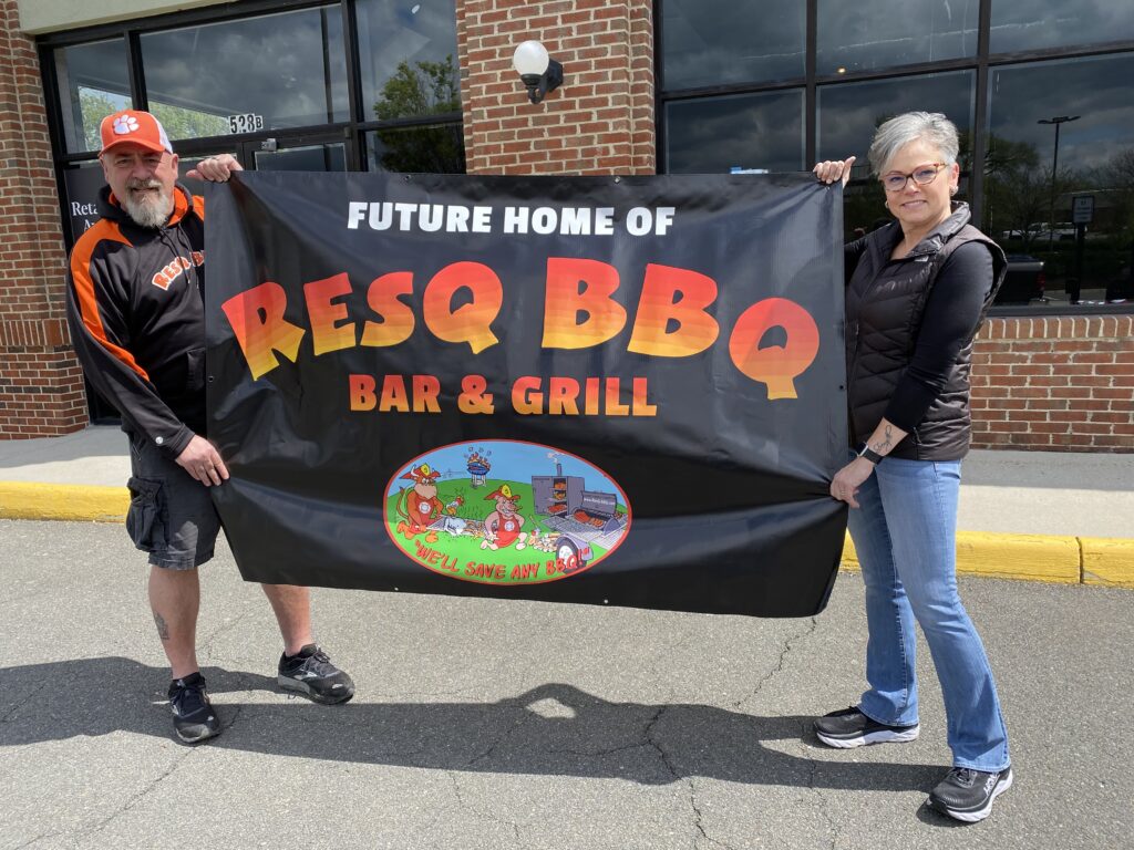 Two people hold a fabric sign saying Future Home of ResQ BBQ Bar and Grill